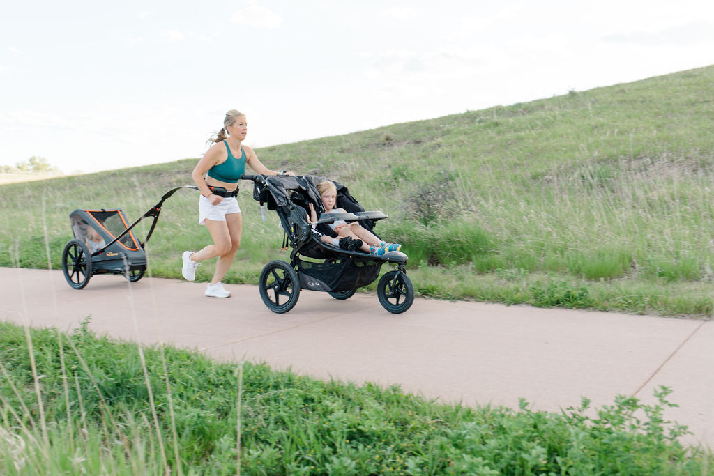 Running postpartum with a stroller, woman pushing a stroller in front of her and has a stroller attached to her as well. 